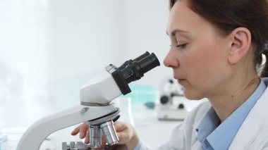 Kadın bilim adamı mikroskop örneklerini analiz ediyor, çağdaş laboratuvar ortamında gelişmiş ekipmanlarla tıbbi tedavileri araştırıyor. Tıp, sağlık ve bilim konsepti