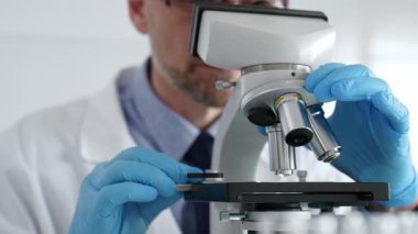 Beyaz önlüklü ve mavi eldivenli, mikroskop ayarlayan, modern laboratuarda ilaç araştırması yapan erkek bilim adamlarına yaklaş. Tıp ve bilim konsepti.