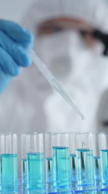 Koruyucu ekipman takan bilim araştırmacısı, tıbbi araştırma deneyi yaparken deney tüplerine sıvıyı dikkatlice yerleştiriyor. Tıp, sağlık ve bilim konsepti.