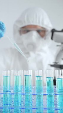 Koruyucu ekipman takan bilim araştırmacısı, tıbbi araştırma deneyi yaparken deney tüplerine sıvıyı dikkatlice yerleştiriyor. Tıp, sağlık ve bilim konsepti.
