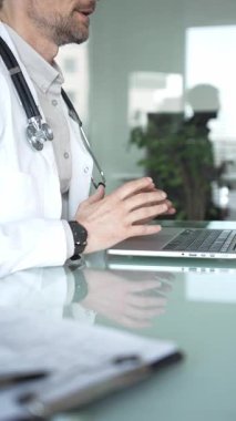 Laboratuvar önlüğü ve steteskop giyen bir doktor cam bir masadaki modern bir dizüstü bilgisayarda yazı yazıyor, sağlık bilgilerini yönetiyor. Tıp, sağlık ve bilim konsepti