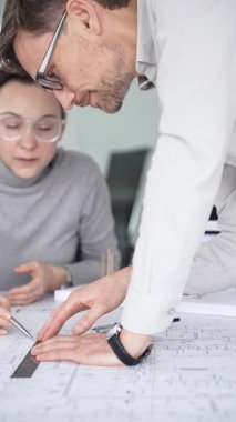 Mimarlar inşaat planlarını ve 3D yapı modelini gözden geçiriyorlar, profesyonel ofis ortamında yeni bir mimari proje üzerinde çalışırken ayrıntılı bir tasarım tartışmasına girişiyorlar.