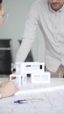 Mimarlar yeni bina tasarımını tartışıyor, ayrıntılı planların üzerinde bir pusula tutuyor, modern bir ofis düzeninde ev mimarisi modeliyle proje geliştirmede işbirliği yapıyor,