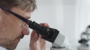 Bir erkek bilim adamının mikroskopla bakıp laboratuvar ortamında araştırma ve analiz yapması bilimsel araştırma ve keşifler sergilemesi. Tıp ve bilim konsepti.