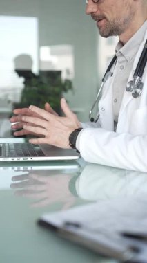 Laboratuvar önlüğü ve steteskop giyen bir doktor cam bir masadaki modern bir dizüstü bilgisayarda yazı yazıyor, sağlık bilgilerini yönetiyor. Tıp, sağlık ve bilim konsepti