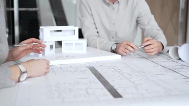 Mimarlık uzmanları proje toplantısı sırasında çağdaş bir ofis ortamında tasarım ayrıntılarını rafine etmek için bir cetvel kullanarak projeler ve ev ölçeği modeli üzerinde işbirliği yaparlar.