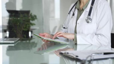 Ofis masasında steteskop kullanan beyaz önlüklü doktor, tele sağlık ve klinik bakım yenilikleri için dijital hasta verilerini inceliyor. İlaç ve sağlık hizmetleri kavramı
