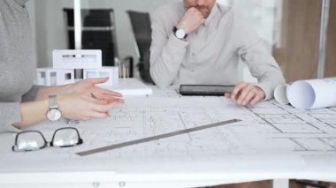 Mimari planlar ve inşaat planları üzerinde işbirliği yapan mimarlar, mühendislik projesinin detaylarını tartışan, bir ofiste tasarım araçları ve dijital tablet kullanan mimarlar