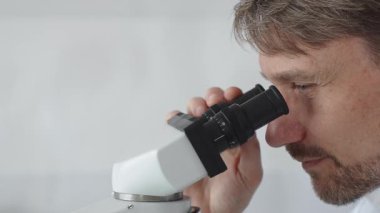 Yeni ilaçlar ve tedaviler geliştirmek için parlak ışıklı bir laboratuvarda mikroskopla gözlem yapan bir bilim adamına yakından bakın. Tıp ve bilim konsepti.