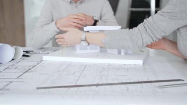 Bir ortaklık kuran iş adamları, mimari planları ve bina modelini el sıkışarak, başarılı bir anlaşmayı ve inşaat endüstrisindeki işbirliğini sembolize ederek,