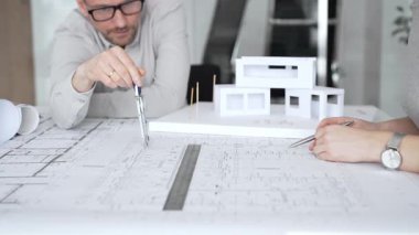 Mimarlık uzmanları proje toplantısı sırasında çağdaş bir ofis ortamında tasarım ayrıntılarını rafine etmek için bir cetvel kullanarak projeler ve ev ölçeği modeli üzerinde işbirliği yaparlar.