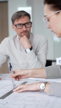 Mimari planlar ve inşaat planları üzerinde işbirliği yapan mimarlar, mühendislik projesinin detaylarını tartışan, bir ofiste tasarım araçları ve dijital tablet kullanan mimarlar