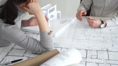 İki mimar yeni bir bina tasarımında işbirliği yapıyor ayrıntılı planları gözden geçiriyorlar ve pusula ile beyaz bir mimari modelin yanındaki planları titizlikle ölçüyorlar.