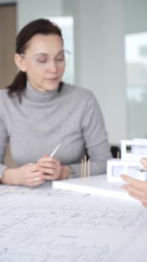 Planlar üzerinde işbirliği yapan mimarlar, kadın bir meslektaşın gözlemlediği gibi planları ölçmek için pusula kullanan bir erkek tasarımcı, proje detayları ve mimari tasarımı tartışan,