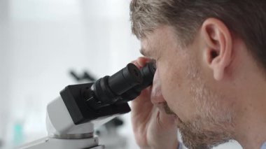 Yeni ilaçlar ve tedaviler geliştirmek için parlak ışıklı bir laboratuvarda mikroskopla gözlem yapan bir bilim adamına yakından bakın. Tıp ve bilim konsepti.