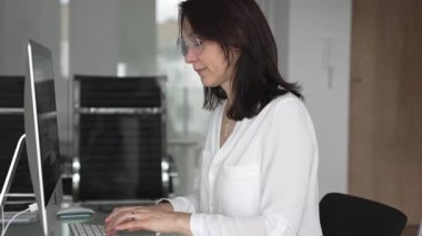 İş kadını verileri yönetir ve çağdaş bir ofiste bilgisayar ekranında finansal grafikleri analiz eder, raporlara ve iş stratejisine odaklanır, üretkenliği ve kurumsal başarıyı temsil eder