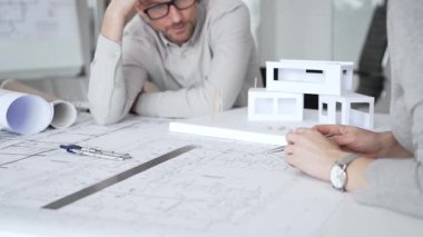 Mimarlık uzmanları proje toplantısı sırasında çağdaş bir ofis ortamında tasarım ayrıntılarını rafine etmek için bir cetvel kullanarak projeler ve ev ölçeği modeli üzerinde işbirliği yaparlar.