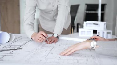 Mimarlar yeni bina tasarımını tartışıyor, ayrıntılı planların üzerinde bir pusula tutuyor, modern bir ofis düzeninde ev mimarisi modeliyle proje geliştirmede işbirliği yapıyor,