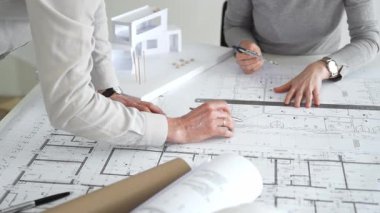 Mimarlar küçük bir ev modelinin ayrıntılı planlarını çizer ve ölçerler, bir konut tasarımı projesi için kesin takım çalışması, planlama ve işbirliği vurgulanır, kapat