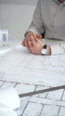 Mimarlar detaylı planlar ve beyaz bir masanın üzerinde bir ölçek modeli etrafında toplanarak, modern bir konut projesinde işbirliği yaparken planları analiz ediyor, araçlar ve belgeler çiziyor ve kapatıyorlar.