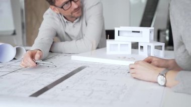 Mimarlık uzmanları proje toplantısı sırasında çağdaş bir ofis ortamında tasarım ayrıntılarını rafine etmek için bir cetvel kullanarak projeler ve ev ölçeği modeli üzerinde işbirliği yaparlar.