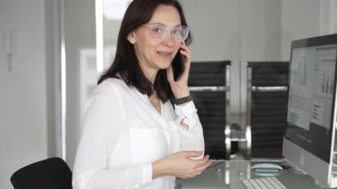 İş kadını büro masasında telefonla konuşuyor, işi yönetiyor, müşterilerle iletişim kuruyor, bilgisayara danışıyor, proje detaylarını tartışıyor, kurumsal sohbete katılıyor. İş adamları konsepti