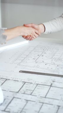 Bir ortaklık kuran iş adamları, mimari planları ve bina modelini el sıkışarak, başarılı bir anlaşmayı ve inşaat endüstrisindeki işbirliğini sembolize ederek,