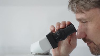 Yeni ilaçlar ve tedaviler geliştirmek için parlak ışıklı bir laboratuvarda mikroskopla gözlem yapan bir bilim adamına yakından bakın. Tıp ve bilim konsepti.