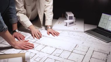 Mimarlar mimari planlara işaret ediyor, bir dizüstü bilgisayarın kaba yazılım ve fiziksel yapı modelinin yer aldığı bir masanın tasarım projesinde işbirliği yapıyorlar.