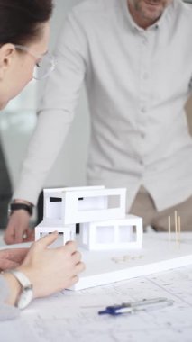 Mimarlar yeni bina tasarımını tartışıyor, ayrıntılı planların üzerinde bir pusula tutuyor, modern bir ofis düzeninde ev mimarisi modeliyle proje geliştirmede işbirliği yapıyor,