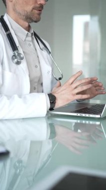 Laboratuvar önlüğü ve steteskop giyen bir doktor cam bir masadaki modern bir dizüstü bilgisayarda yazı yazıyor, sağlık bilgilerini yönetiyor. Tıp, sağlık ve bilim konsepti