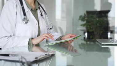 Ofis masasında steteskop kullanan beyaz önlüklü doktor, tele sağlık ve klinik bakım yenilikleri için dijital hasta verilerini inceliyor. İlaç ve sağlık hizmetleri kavramı