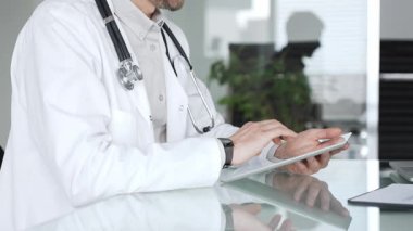 Beyaz önlüklü doktor ve steteskop aktif olarak tablet bilgisayar kullanıyor, dijital sağlık hizmetlerini, sağlık yeniliklerini ve teletıp tedavisini temsil ediyor. Tıp, sağlık ve bilim konsepti