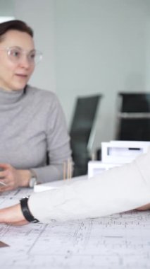 Planlar üzerinde işbirliği yapan mimarlar, kadın bir meslektaşın gözlemlediği gibi planları ölçmek için pusula kullanan bir erkek tasarımcı, proje detayları ve mimari tasarımı tartışan,