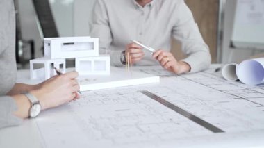 Mimarlık uzmanları proje toplantısı sırasında çağdaş bir ofis ortamında tasarım ayrıntılarını rafine etmek için bir cetvel kullanarak projeler ve ev ölçeği modeli üzerinde işbirliği yaparlar.