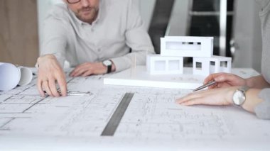 Mimarlık uzmanları proje toplantısı sırasında çağdaş bir ofis ortamında tasarım ayrıntılarını rafine etmek için bir cetvel kullanarak projeler ve ev ölçeği modeli üzerinde işbirliği yaparlar.