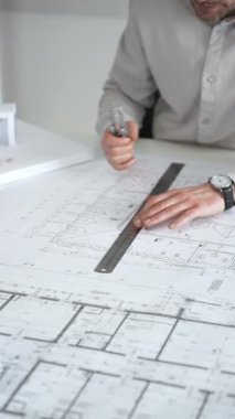 Mimarlar detaylı planlar ve beyaz bir masanın üzerinde bir ölçek modeli etrafında toplanarak, modern bir konut projesinde işbirliği yaparken planları analiz ediyor, araçlar ve belgeler çiziyor ve kapatıyorlar.