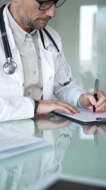 Steteskoplu beyaz önlüklü bir doktor klinikte tıbbi bakım ve profesyonel hizmetler sağlayan bir belge hazırlıyor. Tıp, sağlık ve bilim konsepti