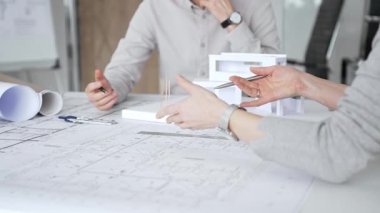 Bir konut projesinde işbirliği yapan mimarlar, planlar ve ölçekli bir modeli bir masada inceleyerek, tasarım detaylarını, inşaat planlarını ve gelecekteki gelişimi tartışarak,