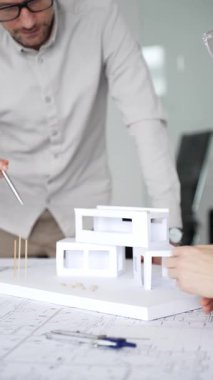Mimarlar yeni bina tasarımını tartışıyor, ayrıntılı planların üzerinde bir pusula tutuyor, modern bir ofis düzeninde ev mimarisi modeliyle proje geliştirmede işbirliği yapıyor,