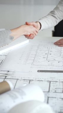 Bir ortaklık kuran iş adamları, mimari planları ve bina modelini el sıkışarak, başarılı bir anlaşmayı ve inşaat endüstrisindeki işbirliğini sembolize ederek,