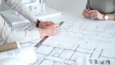 Mimarlar karmaşık bir masa üzerinde ayrıntılı planlar ve beyaz ölçekli bir model üzerinde işbirliği yaparlar, bir inşaat projesi planlarlar ve profesyonel bir tasarım toplantısı sırasında fikirleri paylaşırlar, kapatırlar