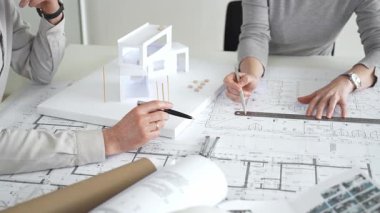 Mimarlar proje planları üzerinde işbirliği yapıyor, mimari tasarımları tartışıyor, inşaat planları geliştiriyor, ofis masasında kavramsal bir model ev yaratıyor, kapatıyorlar.