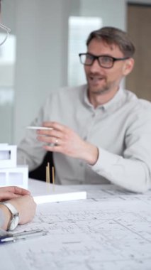 Mimari planlar ve inşaat planları üzerinde işbirliği yapan mimarlar, mühendislik projesinin detaylarını tartışan, bir ofiste tasarım araçları ve dijital tablet kullanan mimarlar