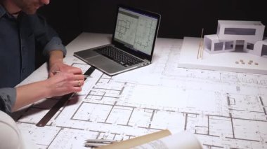 Yeni bir konut geliştirme projesinin planlarını çizen mimar, modern ofis ortamında detaylı ev planları üzerinde çalışarak, inşaat için yenilikçi mimari tasarımlar yaratıyor