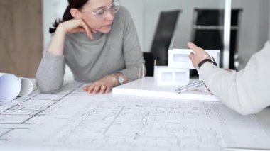 Mimarlar inşaat planlarını ve 3D yapı modelini gözden geçiriyorlar, profesyonel ofis ortamında yeni bir mimari proje üzerinde çalışırken ayrıntılı bir tasarım tartışmasına girişiyorlar.