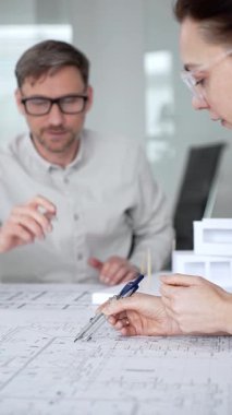 Mimari planlar ve inşaat planları üzerinde işbirliği yapan mimarlar, mühendislik projesinin detaylarını tartışan, bir ofiste tasarım araçları ve dijital tablet kullanan mimarlar