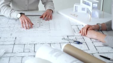 Mimarlar karmaşık bir masa üzerinde ayrıntılı planlar ve beyaz ölçekli bir model üzerinde işbirliği yaparlar, bir inşaat projesi planlarlar ve profesyonel bir tasarım toplantısı sırasında fikirleri paylaşırlar, kapatırlar