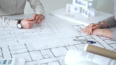 Mimarlar karmaşık bir masa üzerinde ayrıntılı planlar ve beyaz ölçekli bir model üzerinde işbirliği yaparlar, bir inşaat projesi planlarlar ve profesyonel bir tasarım toplantısı sırasında fikirleri paylaşırlar, kapatırlar