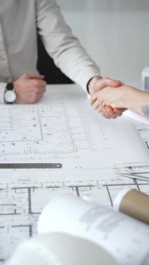 Bir ortaklık kuran iş adamları, mimari planları ve bina modelini el sıkışarak, başarılı bir anlaşmayı ve inşaat endüstrisindeki işbirliğini sembolize ederek,